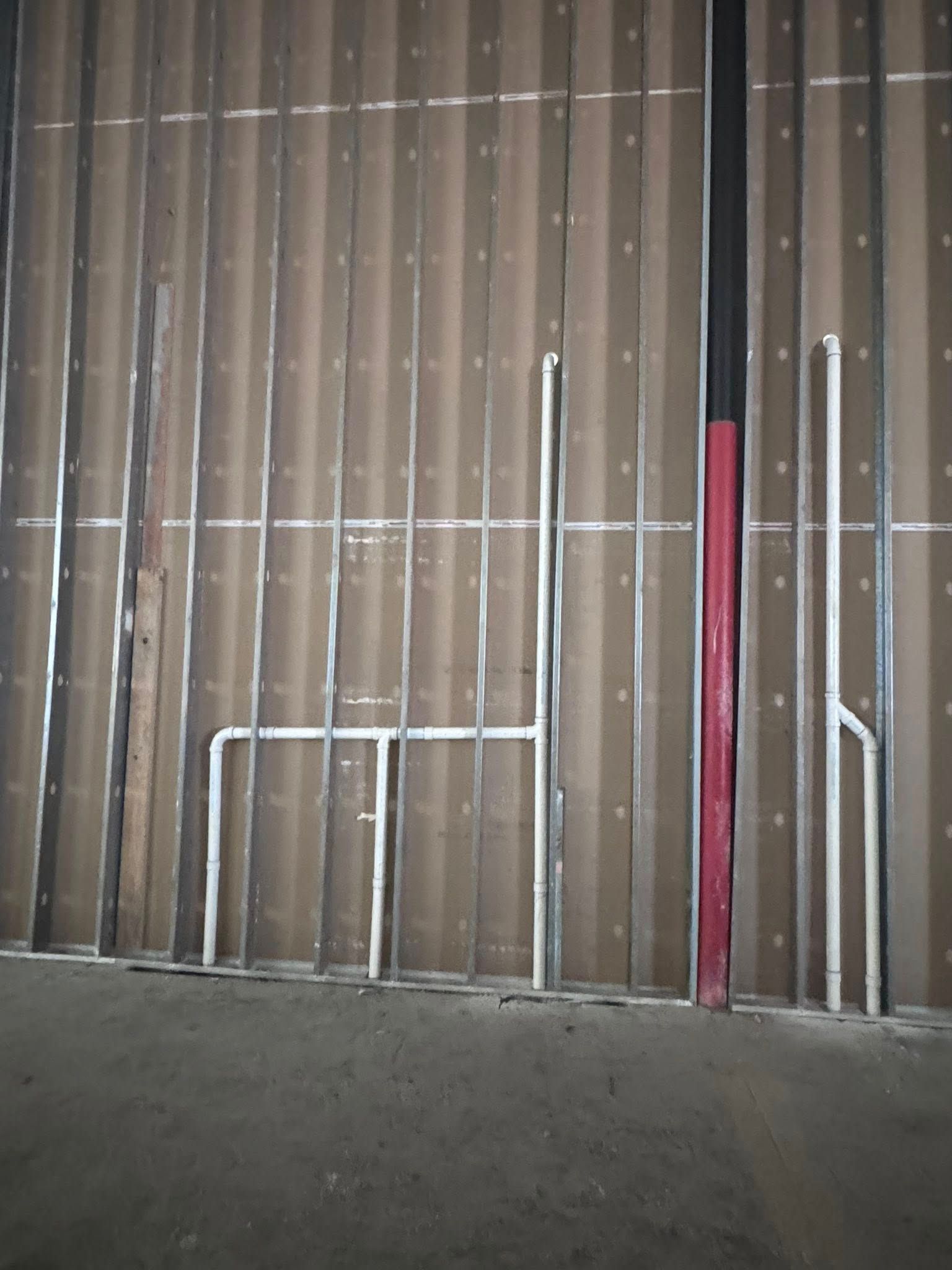 Partially framed wall with exposed studs, vertical red beam, and gray concrete floor.