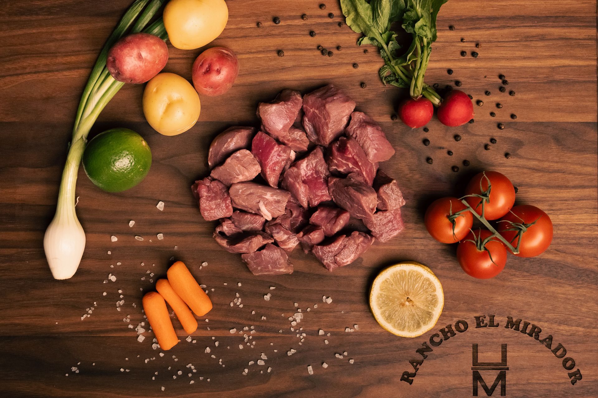 A wooden table topped with meat , vegetables and rancho el mirador logo