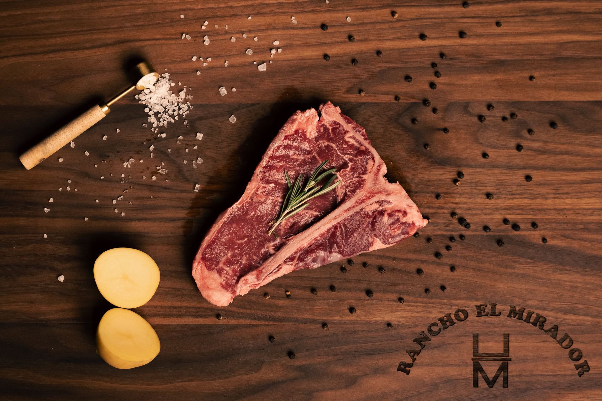 A piece of raw meat is sitting on a wooden table next to potatoes.