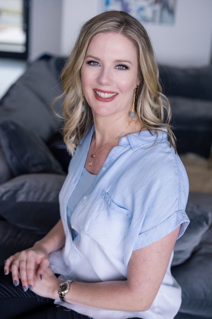 Smiling woman seated on a gray couch, wearing a light blue blouse in a softly lit room