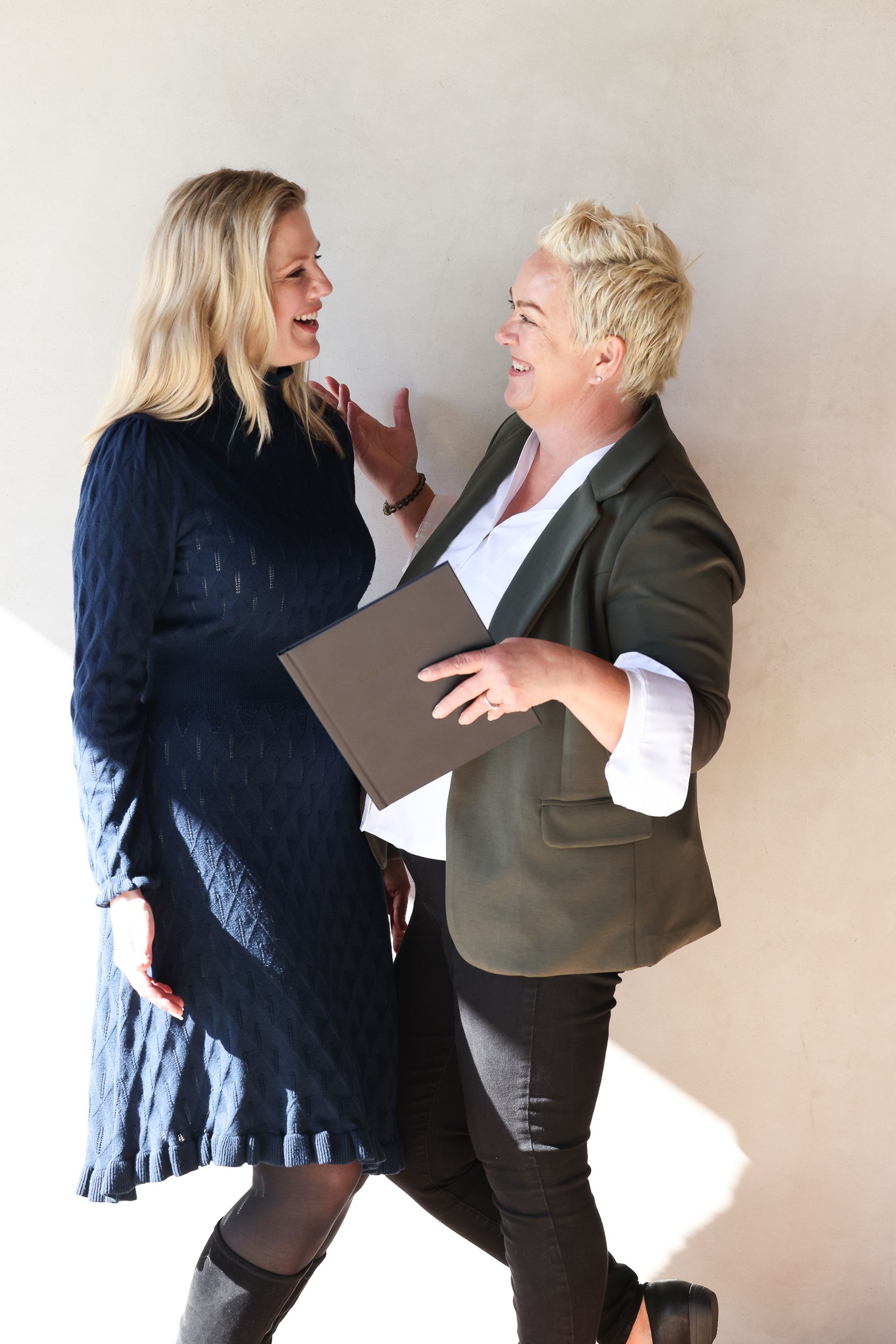 Two people standing close, talking and smiling, one holding a folder in a bright room.