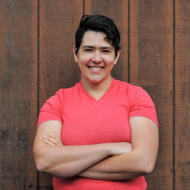 A woman in a red shirt is smiling with her arms crossed