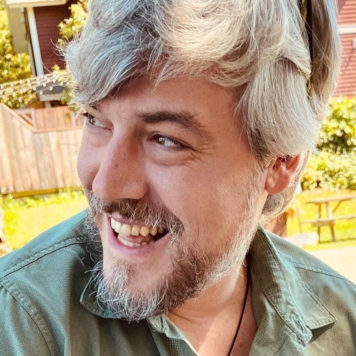 A man with a beard is smiling and wearing a green shirt.