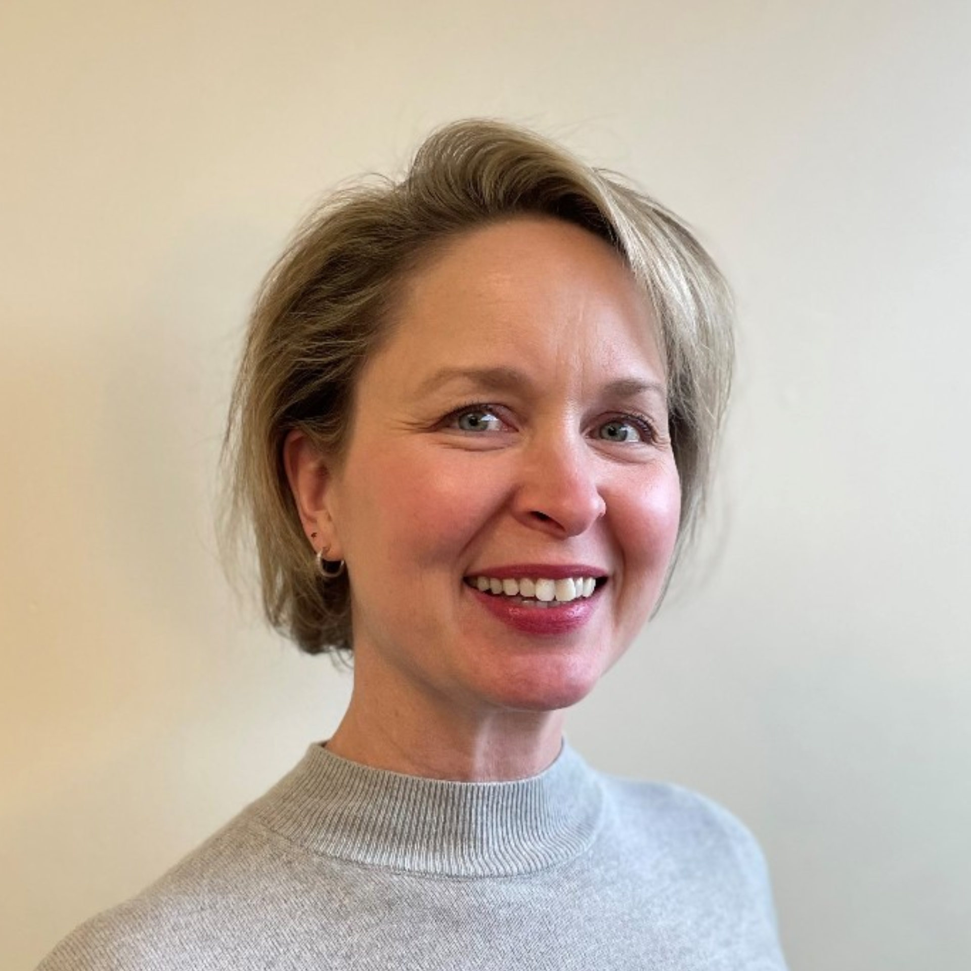 A woman in a grey sweater is smiling for the camera.