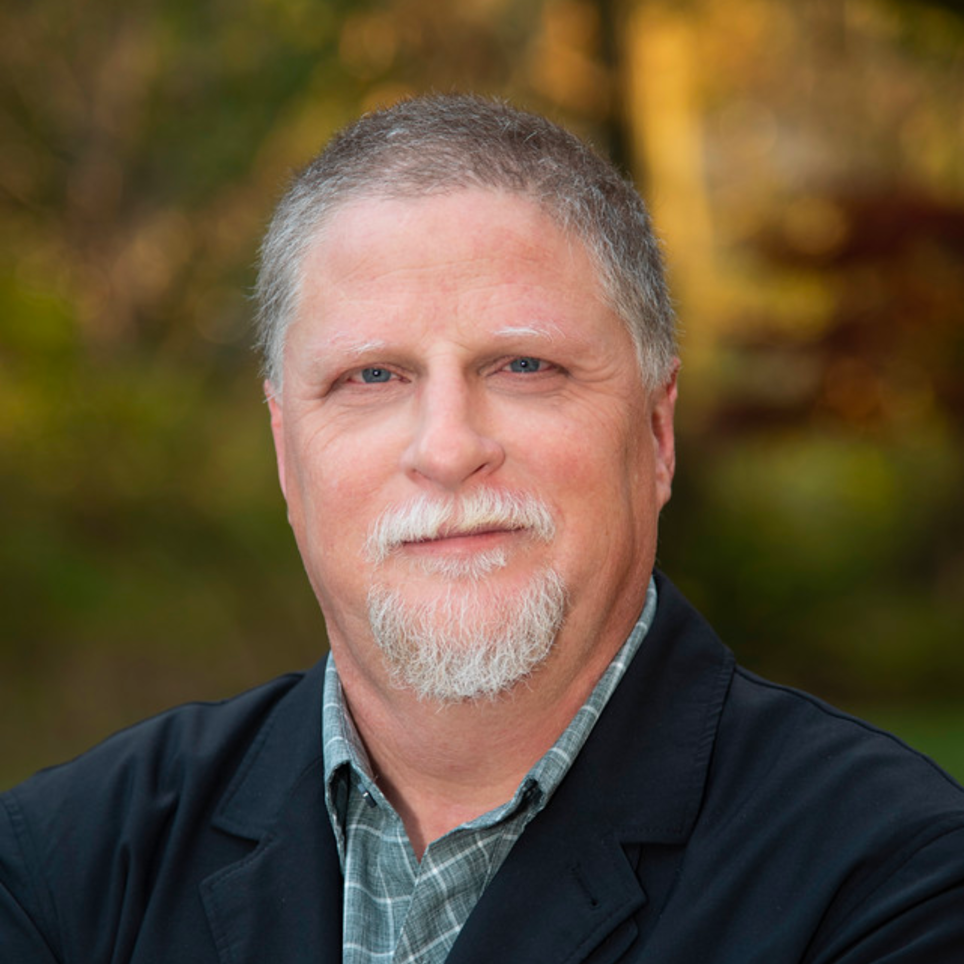 A man with a beard is wearing a black jacket and a plaid shirt.