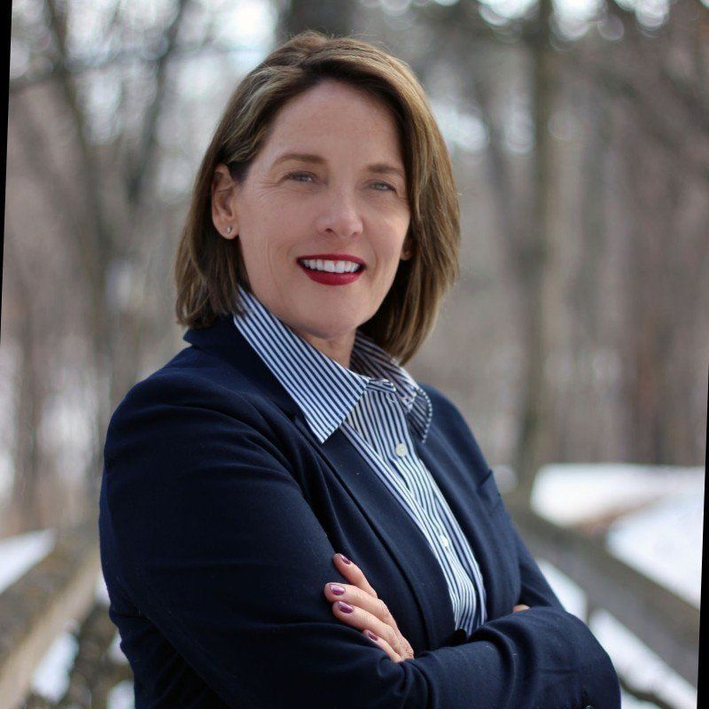 A woman in a suit and striped shirt is smiling with her arms crossed