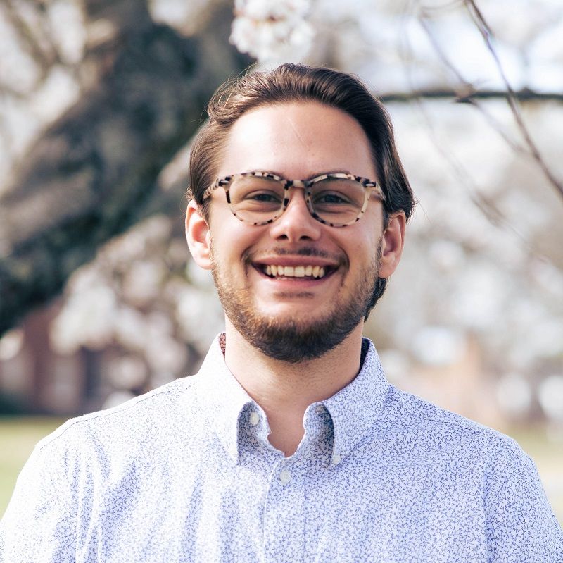 A man wearing glasses and a white shirt is smiling