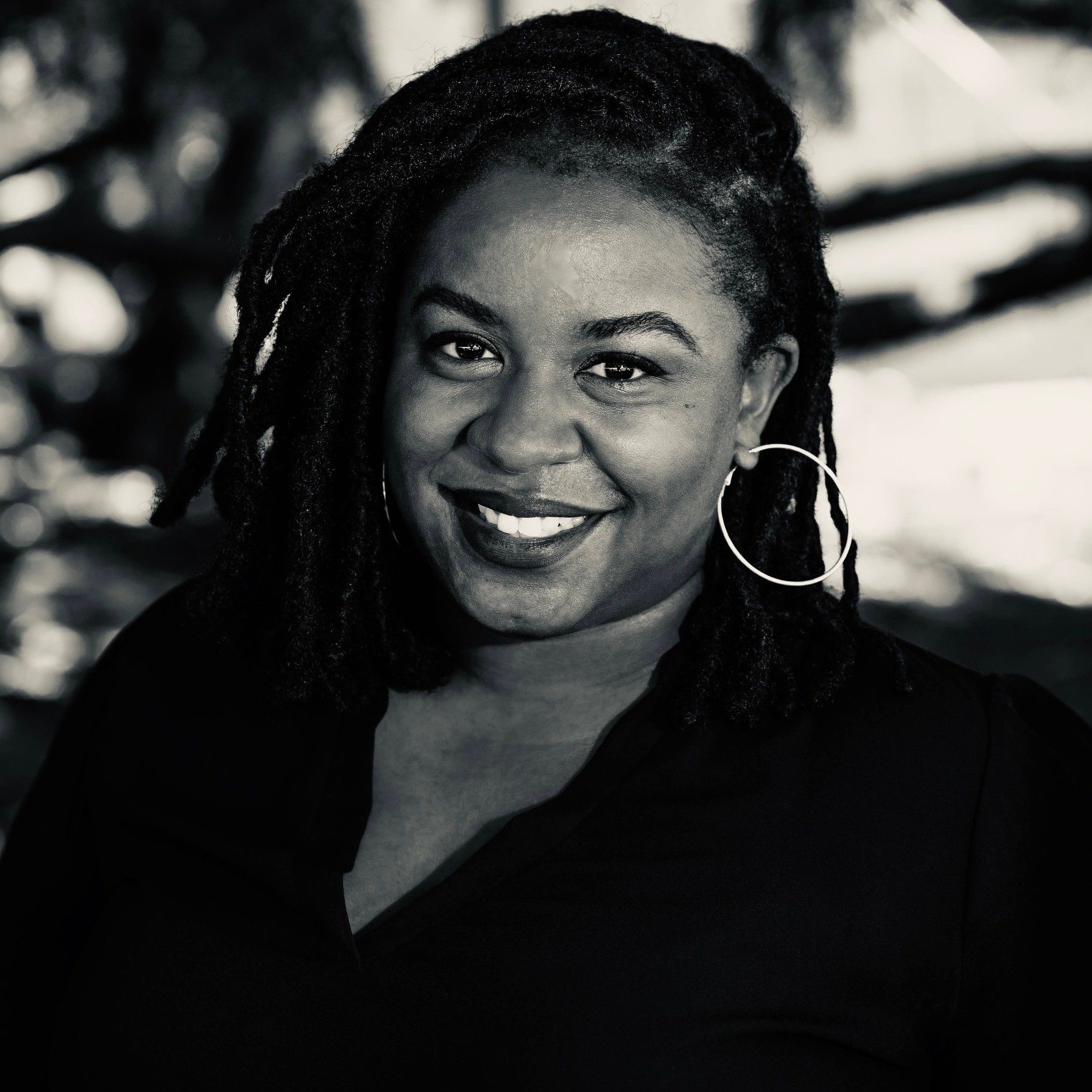A woman with dreadlocks and hoop earrings is smiling in a black and white photo.