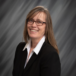 A woman wearing glasses and a black suit is smiling for the camera.