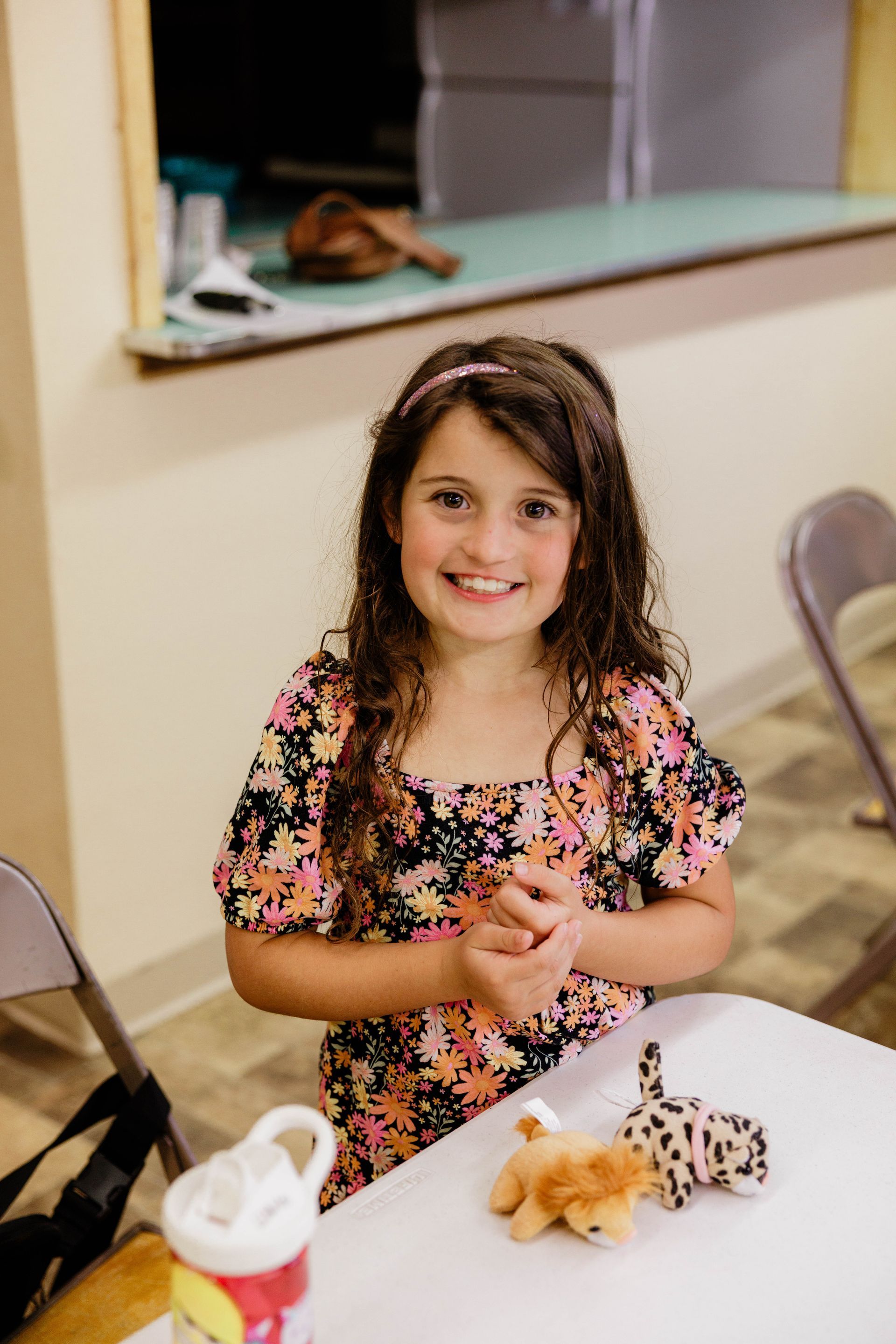 Smiling child in a floral dress at a table with small animal toys and a bottle of bubbles