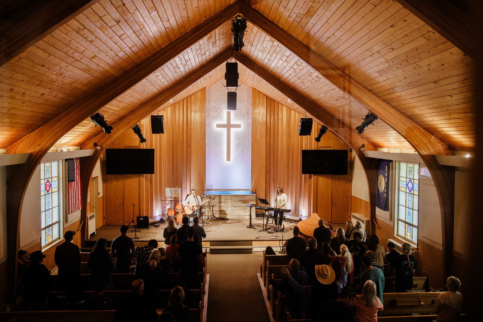 Congregation seated in a wooden church sanctuary with a lit cross at the altar