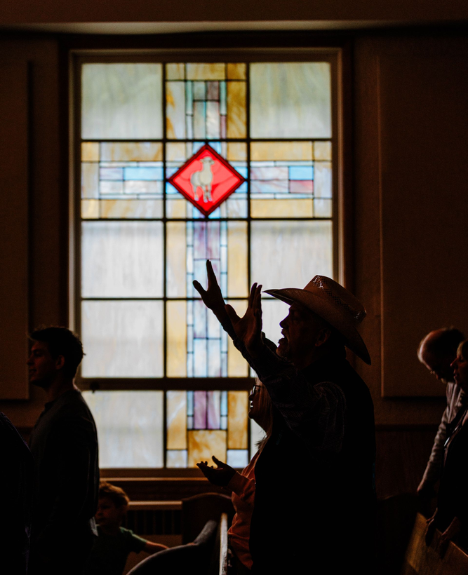 Silhouetted people raising hands before a stained-glass window with a red diamond shape.