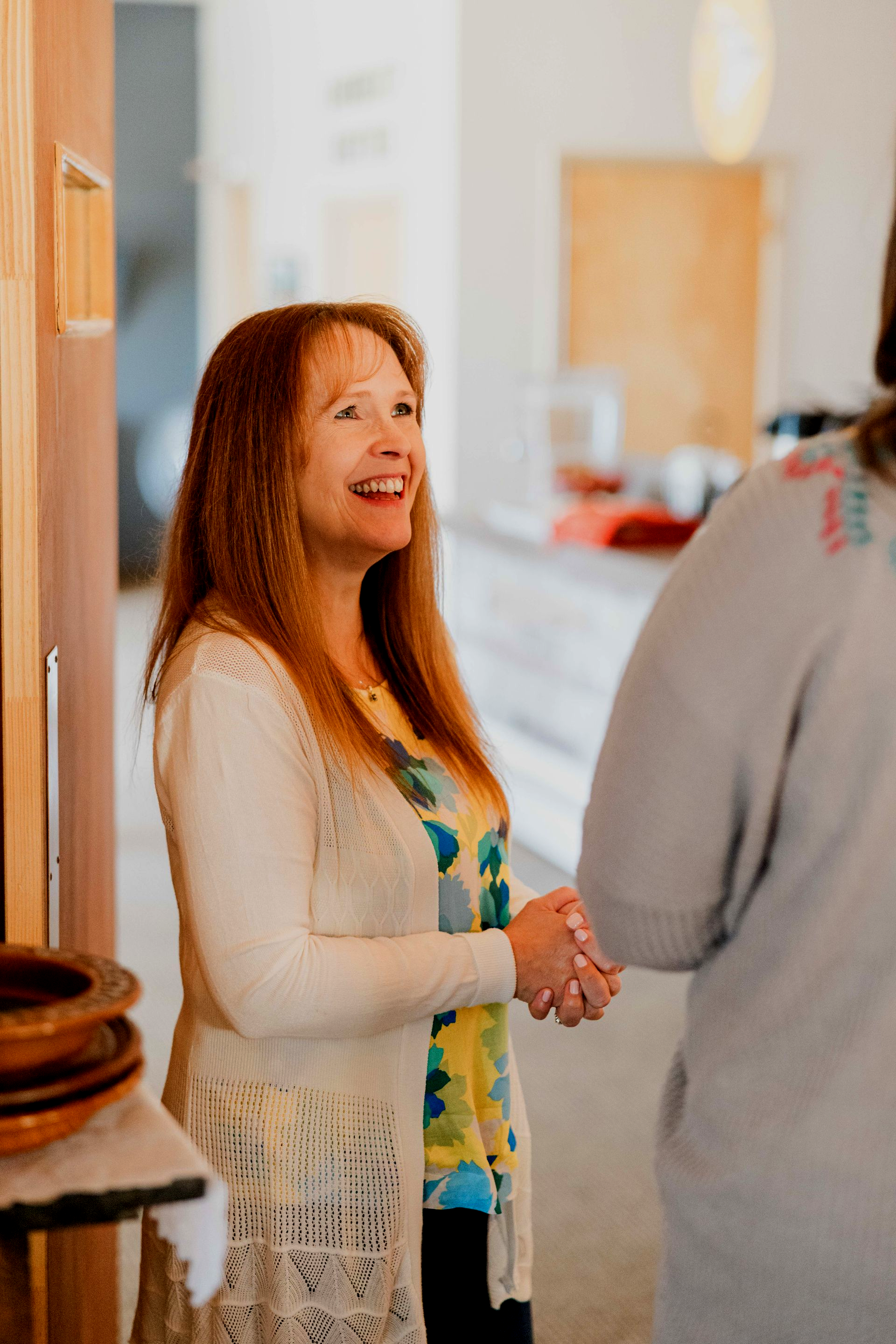 Woman in a white cardigan shaking hands and smiling in a bright indoor hallway