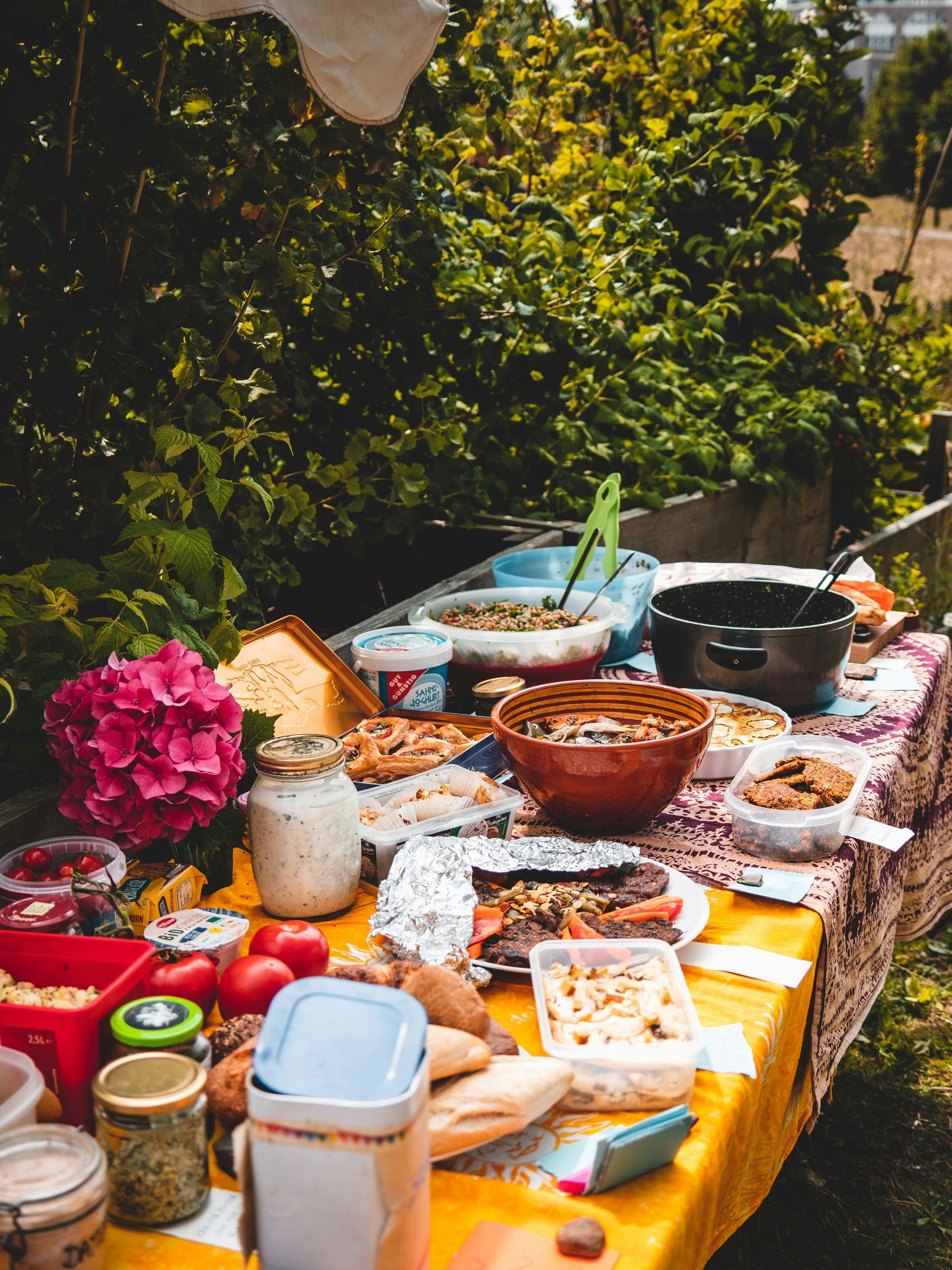 Food potluck items on an outdoor table surrounded by trees