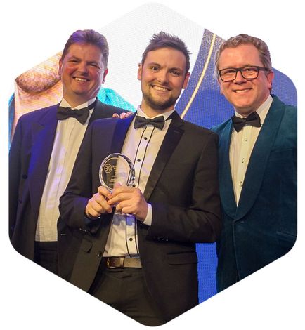Three men in tuxedos smiling and holding an award on stage
