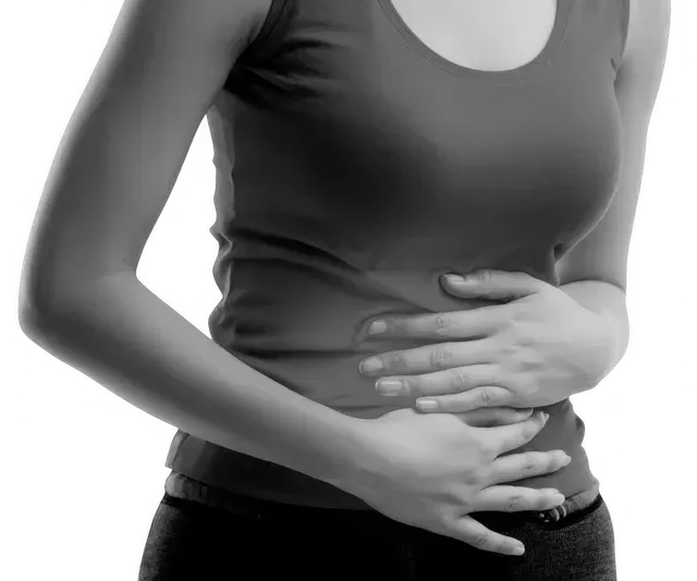 Woman holding her stomach, likely in pain, wearing a tank top and dark pants.
