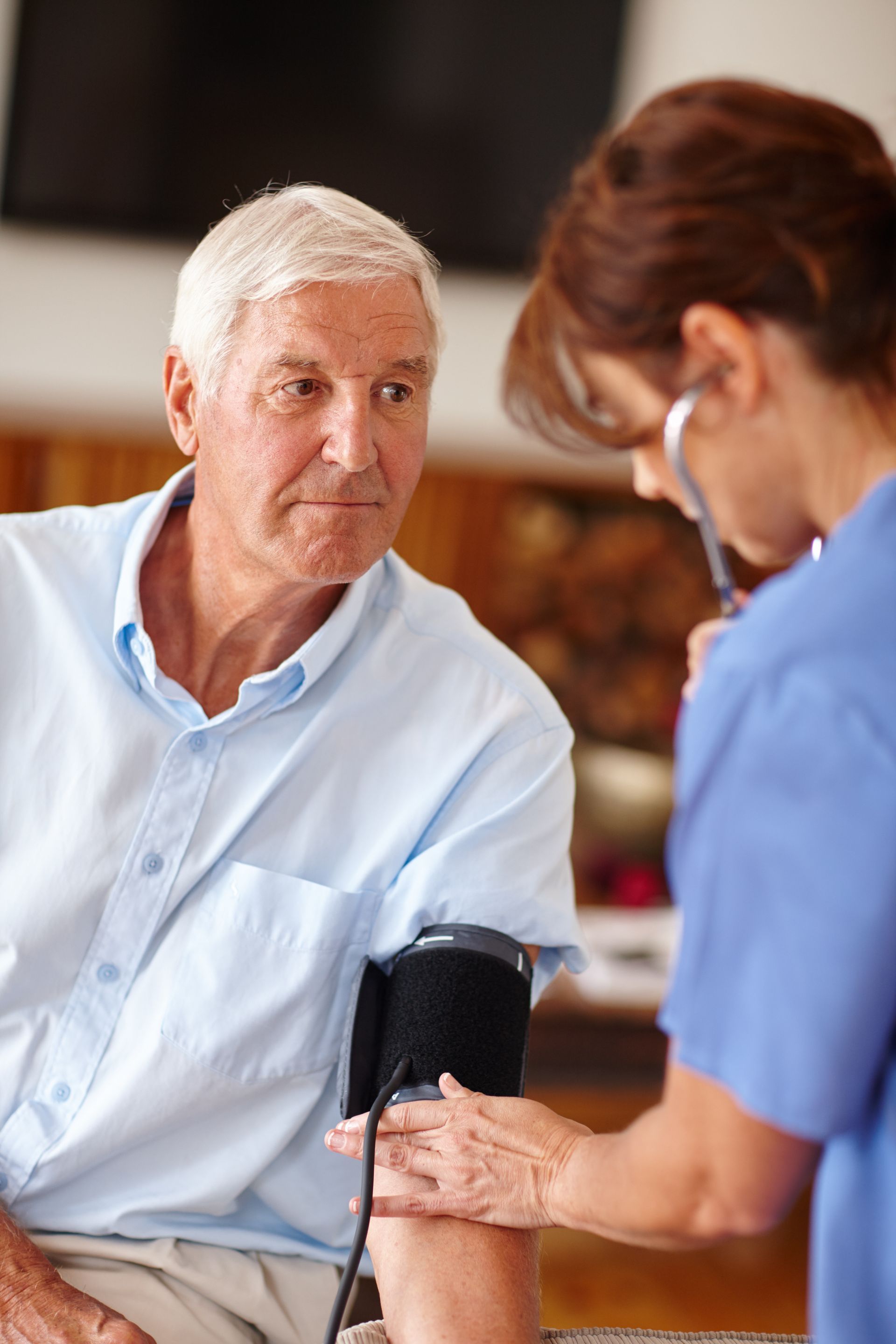 A medical professional taking an older person's blood pressure with a stethoscope.