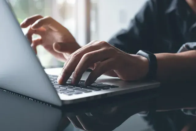 Person typing on a laptop, hands on keyboard.