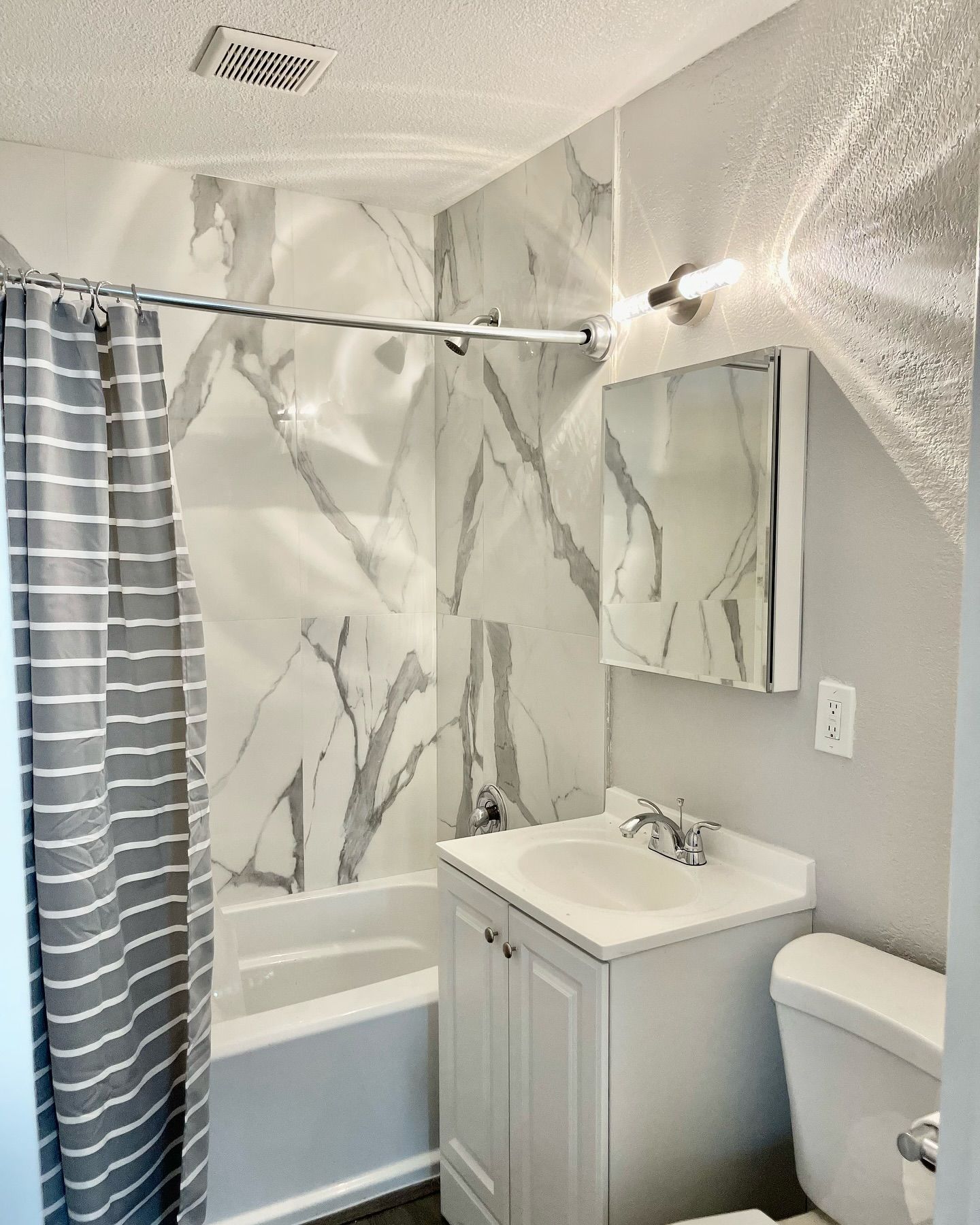 Bathroom with white marble-look tile, shower curtain, vanity, mirror, and toilet. Gray and white color scheme.