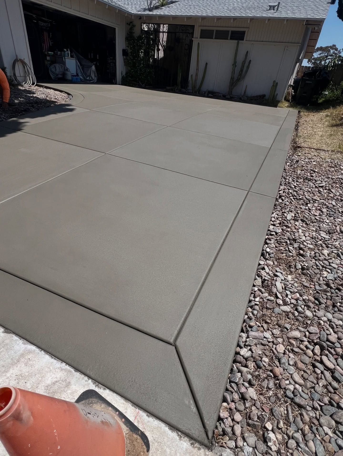 Freshly poured concrete driveway, bordered by rocks, leading to a house with a garage.