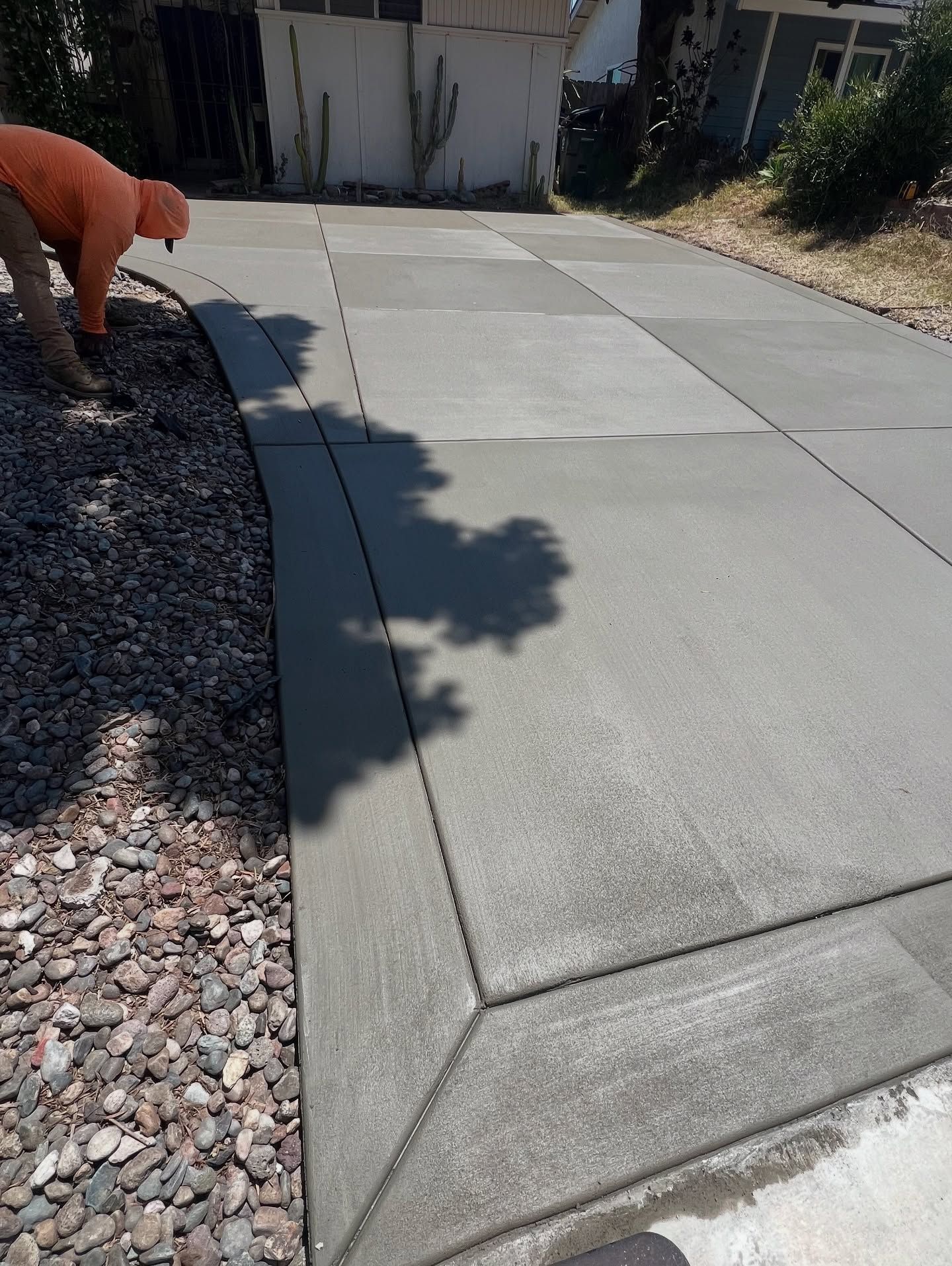 Newly poured concrete driveway with a worker in orange clothing spraying it.