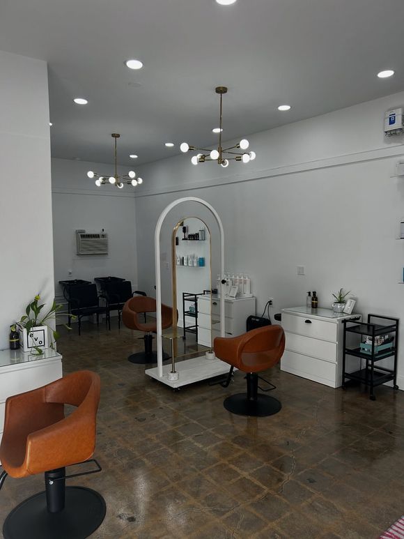 A hair salon interior with chairs, mirrors, and modern lighting fixtures against white walls.