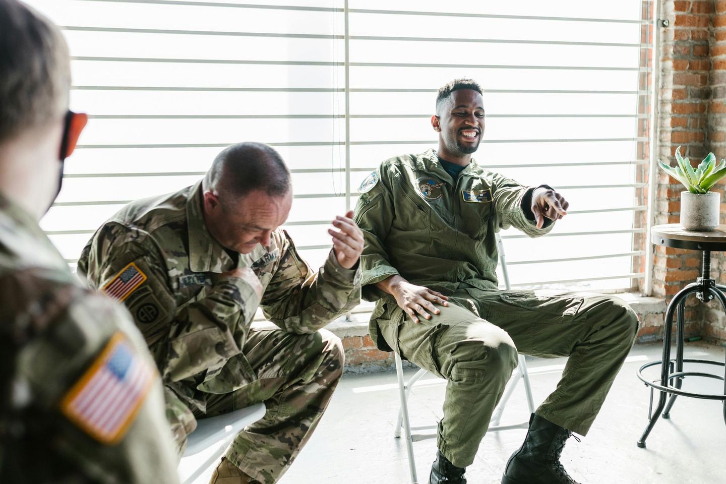 Three soldiers in camouflage uniforms sitting and laughing in a bright room