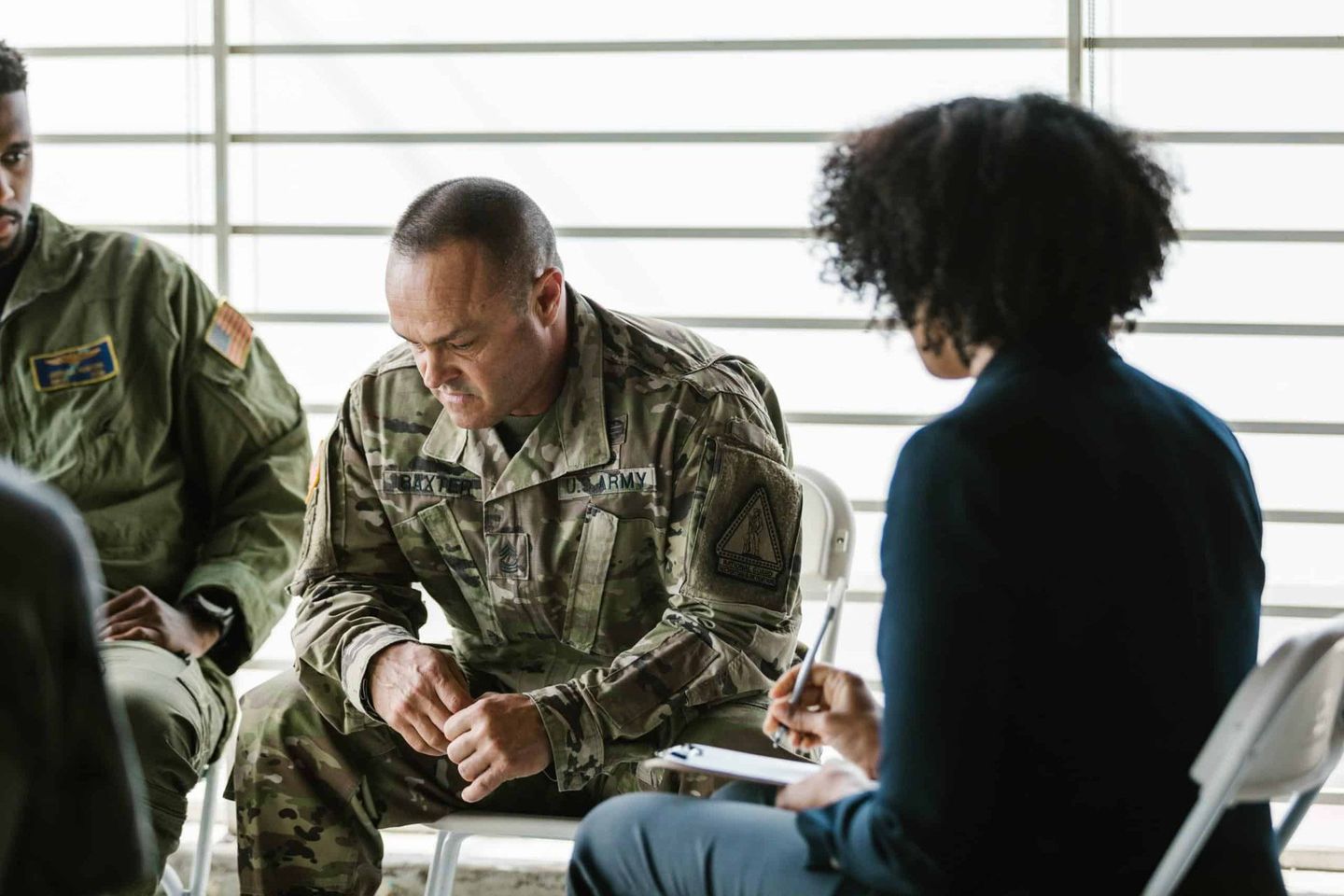 Military personnel and a civilian in discussion during a seated meeting indoors