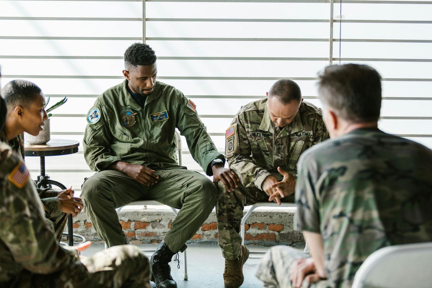 Military personnel sit in a circle during a discussion in a bright room.