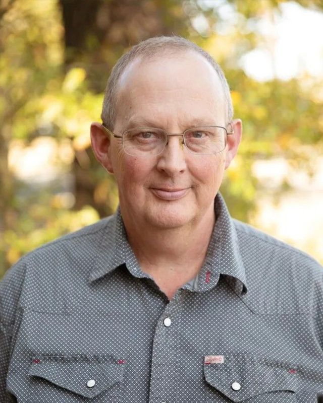 A man wearing glasses and a polka dot shirt is smiling for the camera.
