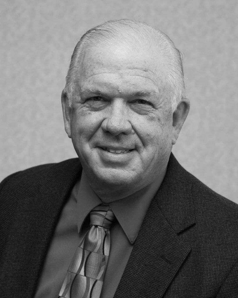 A man in a suit and tie is smiling in a black and white photo.
