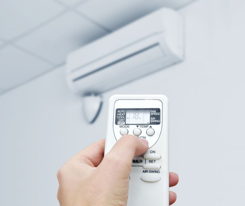 Hand using remote to adjust wall-mounted air conditioner, showing display with settings.