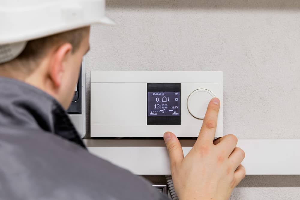 A person in a hard hat adjusting a white thermostat mounted on a wall.