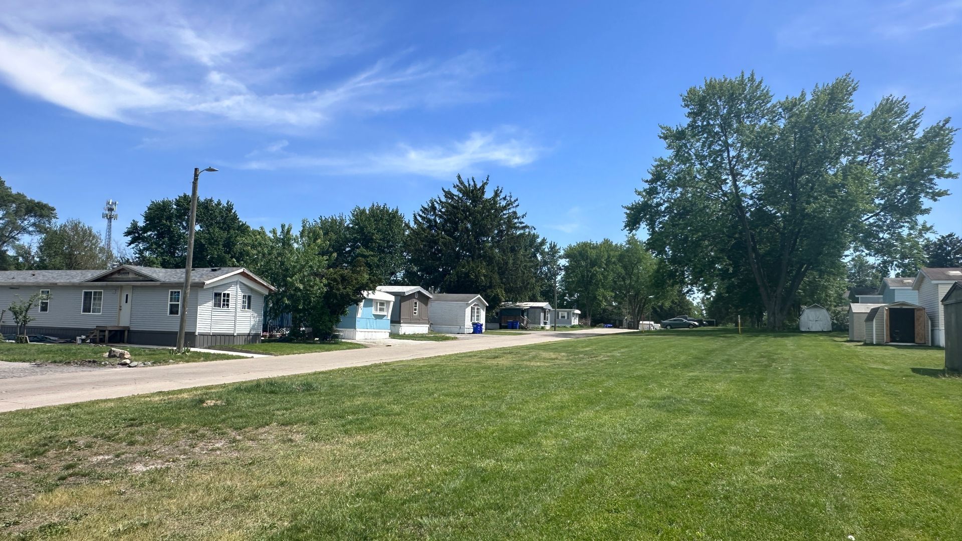 Quiet suburban street with small houses and a wide green lawn under a clear blue sky