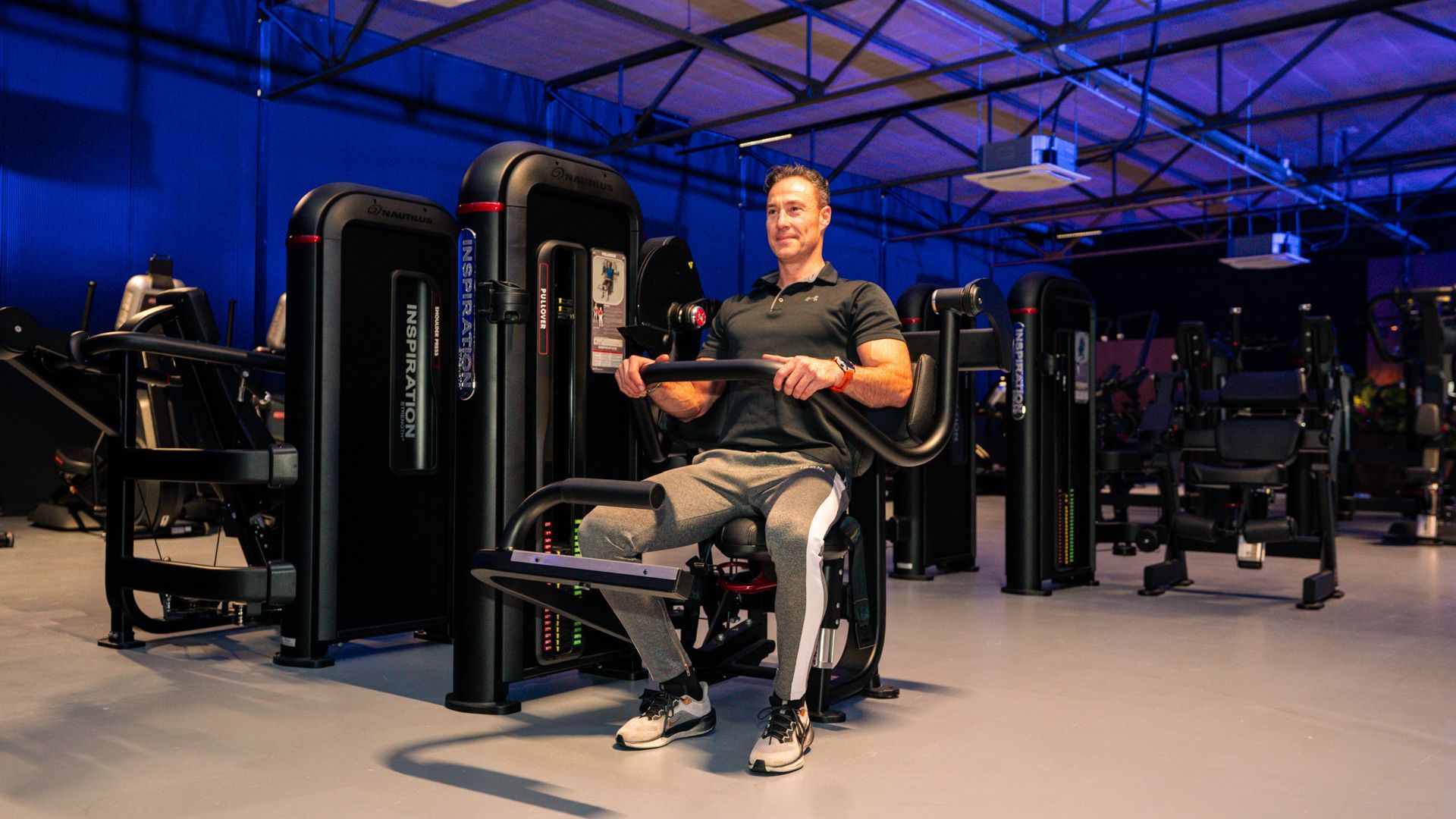 Interieur van een sportschool met loopbanden, halterbanken en gewichten bij de ramen.