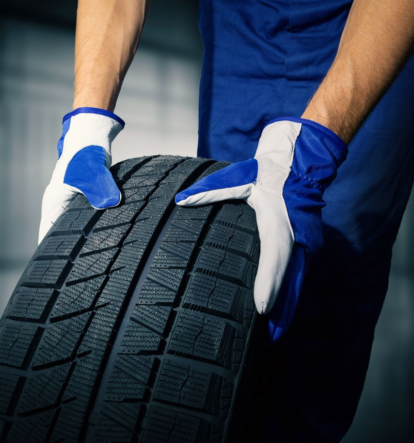 Gloved mechanic holding a car tire with deep tread pattern