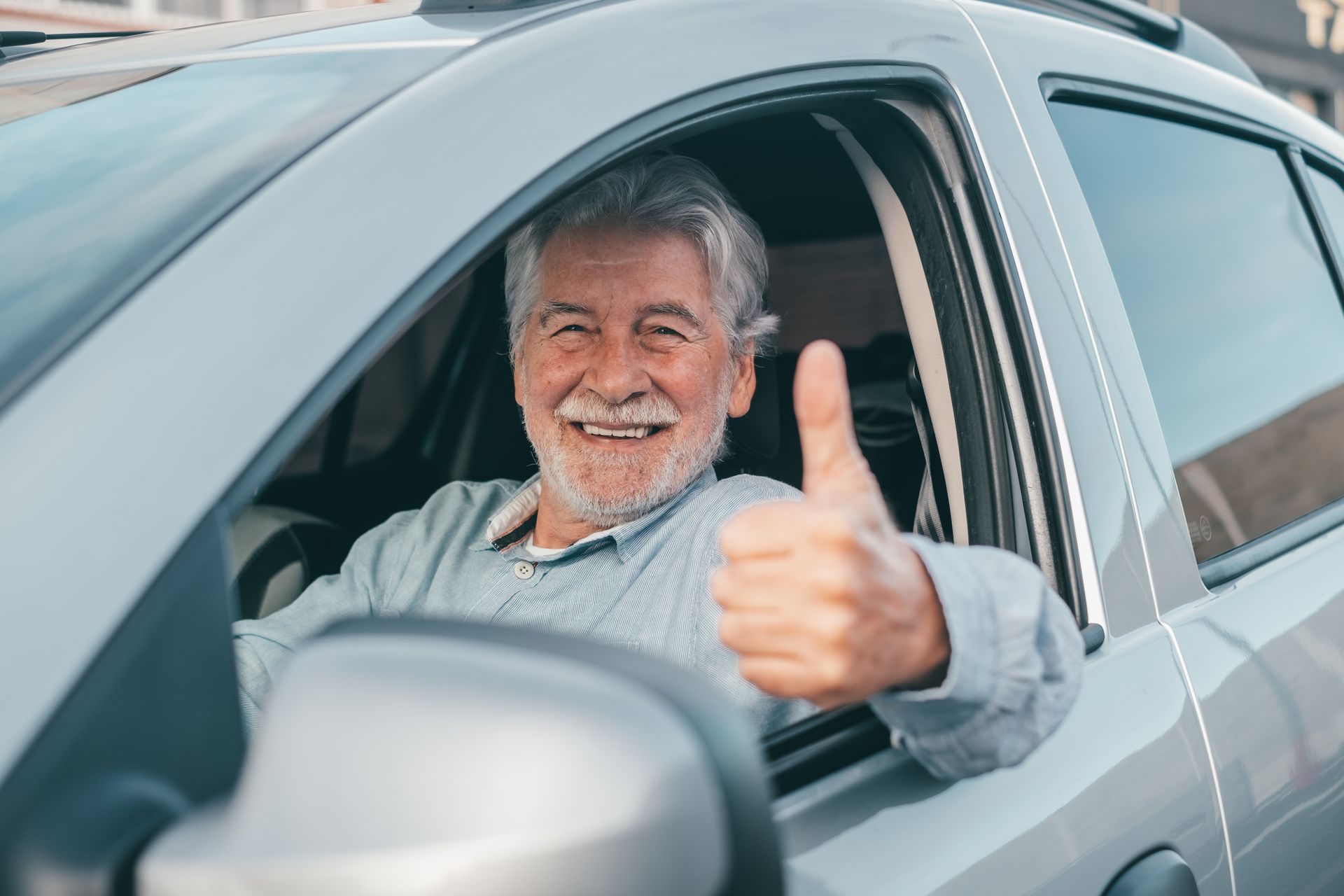 Smiling man in a silver car giving a thumbs-up through the open window
