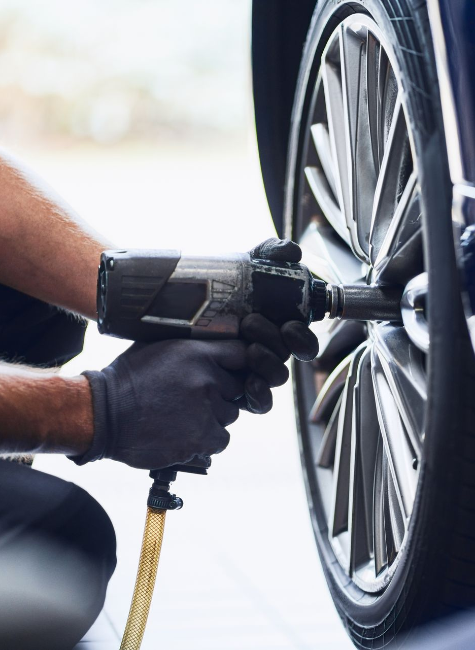 Person using a power tool to remove a car wheel lug nut, close-up on the tire.