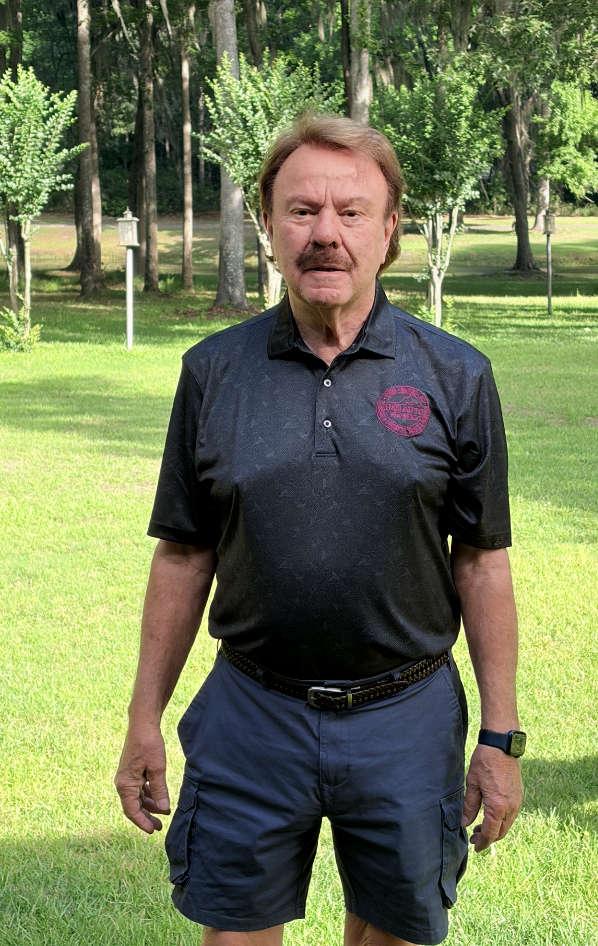 Man in a red polo shirt standing indoors in front of framed artwork, smiling at the camera.