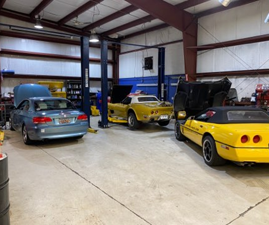 Three classic cars in a workshop, including a yellow Corvette with open hood and doors.