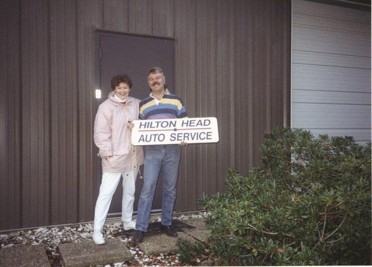 Two people standing by a “Hilton Head Auto Service” sign outside a building