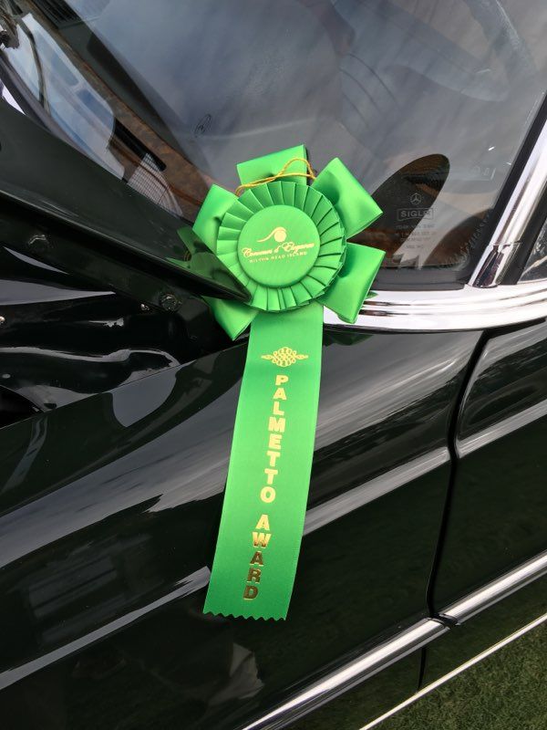 Green ribbon award on a black car door handle with yellow text and rosette badge.