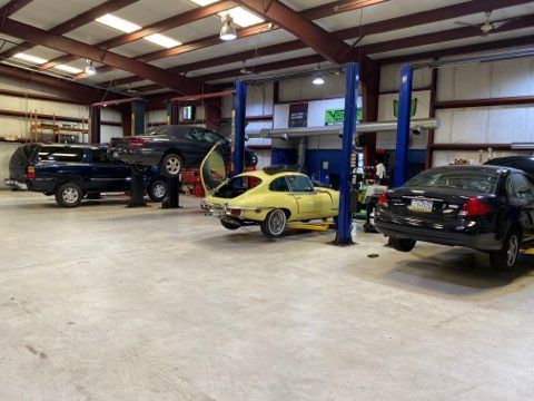 Auto shop interior with several cars on lifts, including a yellow sports car and black SUVs