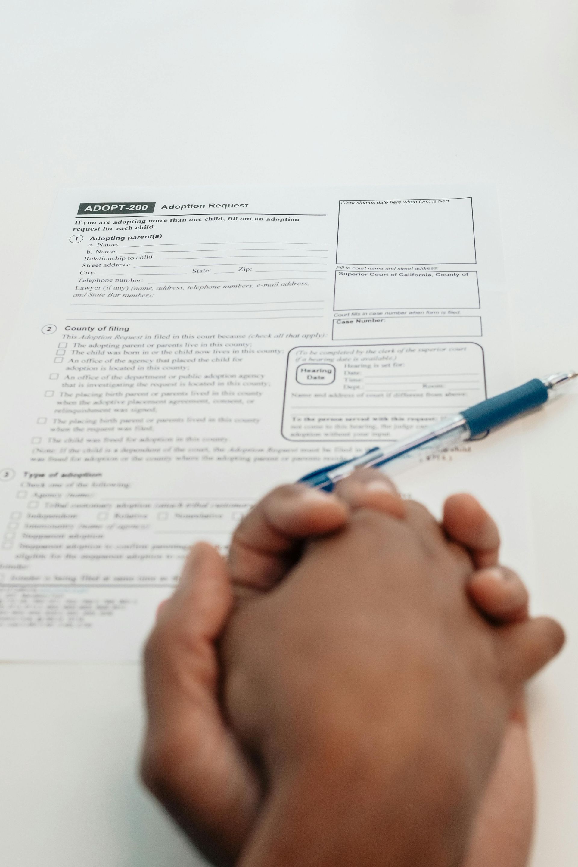 Hands clasped over paperwork with a pen.