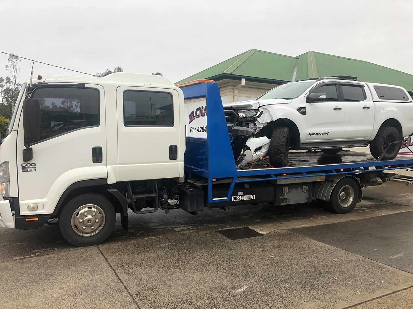 A Tow Truck is Carrying a Damaged White Truck — Quick Hitch Towing & Tilt Tray Services Illawarra in Oak Flats, NSW