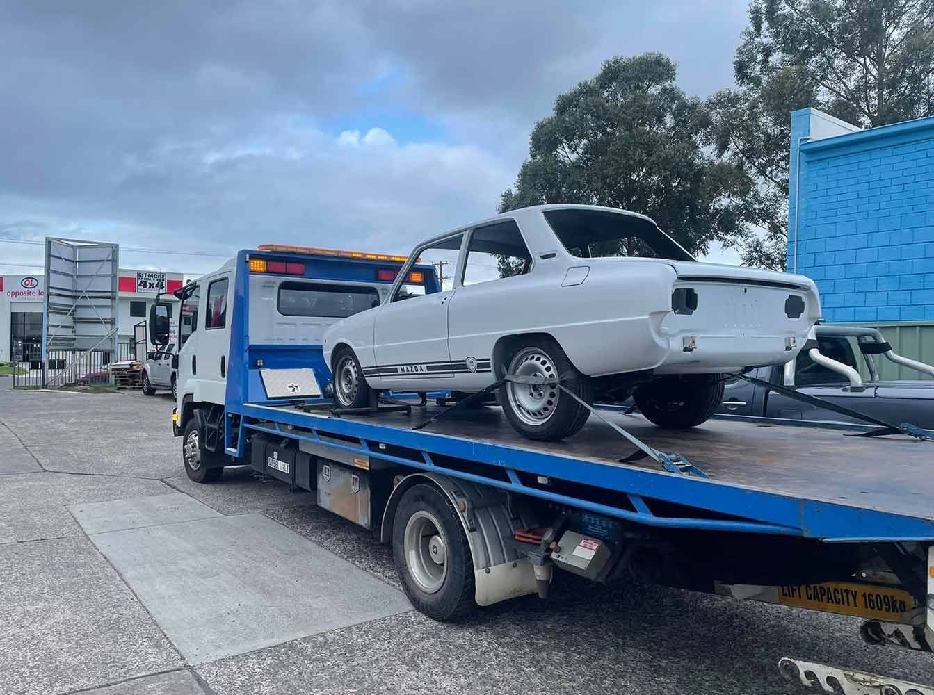 A White Car is Being Towed by a Tow Truck — Quick Hitch Towing & Tilt Tray Services Illawarra in Oak Flats, NSW