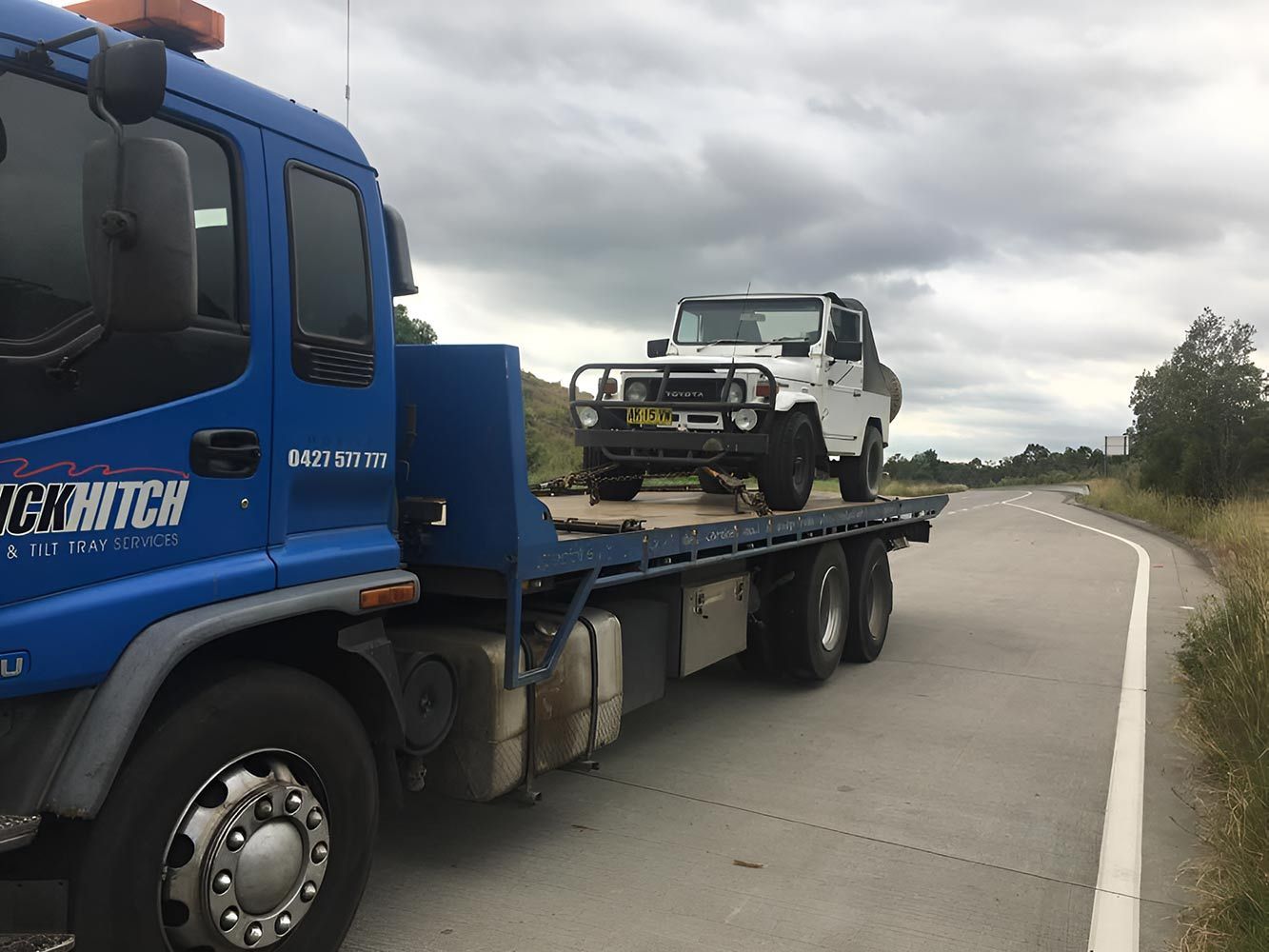 A Blue Tow Truck is Towing a White Jeep Down a Road — Quick Hitch Towing & Tilt Tray Services Illawarra in Port Kembla, NSW