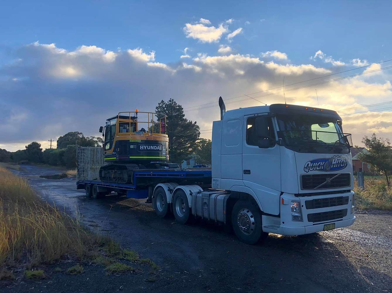 A White Truck is Towing a Yellow Excavator — Quick Hitch Towing & Tilt Tray Services Illawarra in Oak Flats, NSW