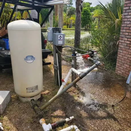 Water softener tanks and plumbing pipes in an outdoor utility area after heavy rain.