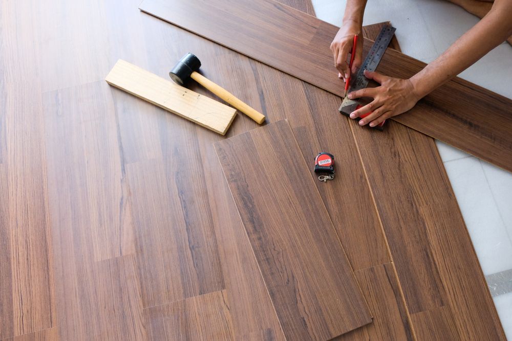Person cutting and measuring wood flooring with a ruler, hammer and block nearby.